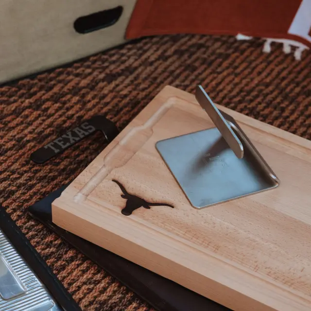 A wooden sundial with a gnomon shadow indicating the time, accompanied by a 'TEXAS' labeled bookmark, on a textured surface.