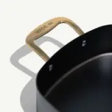 A high-quality, dark non-stick pot features a brass handle marked with "MADE IN."