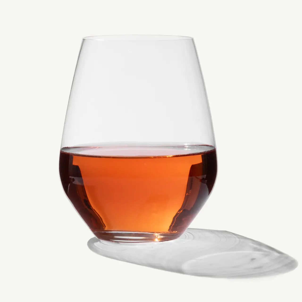 A tilted glass of whiskey with spilled liquid forming a puddle on the surface below it.