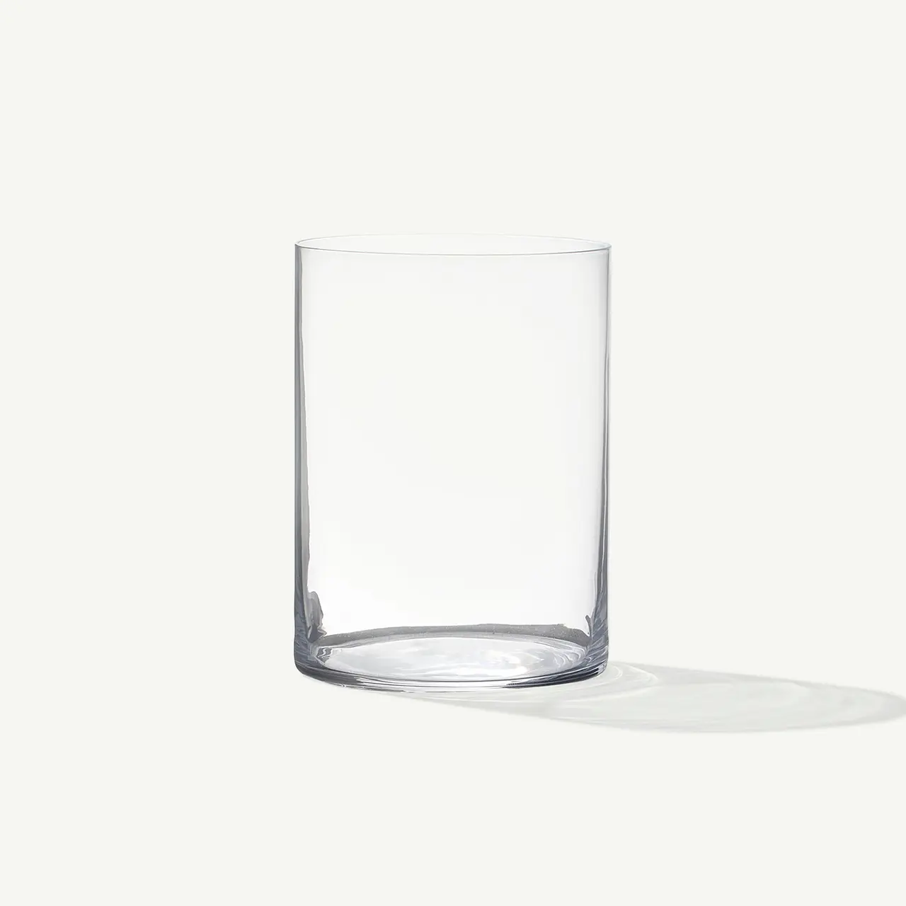 An empty clear glass is standing upright on a pale background, casting a soft shadow.
