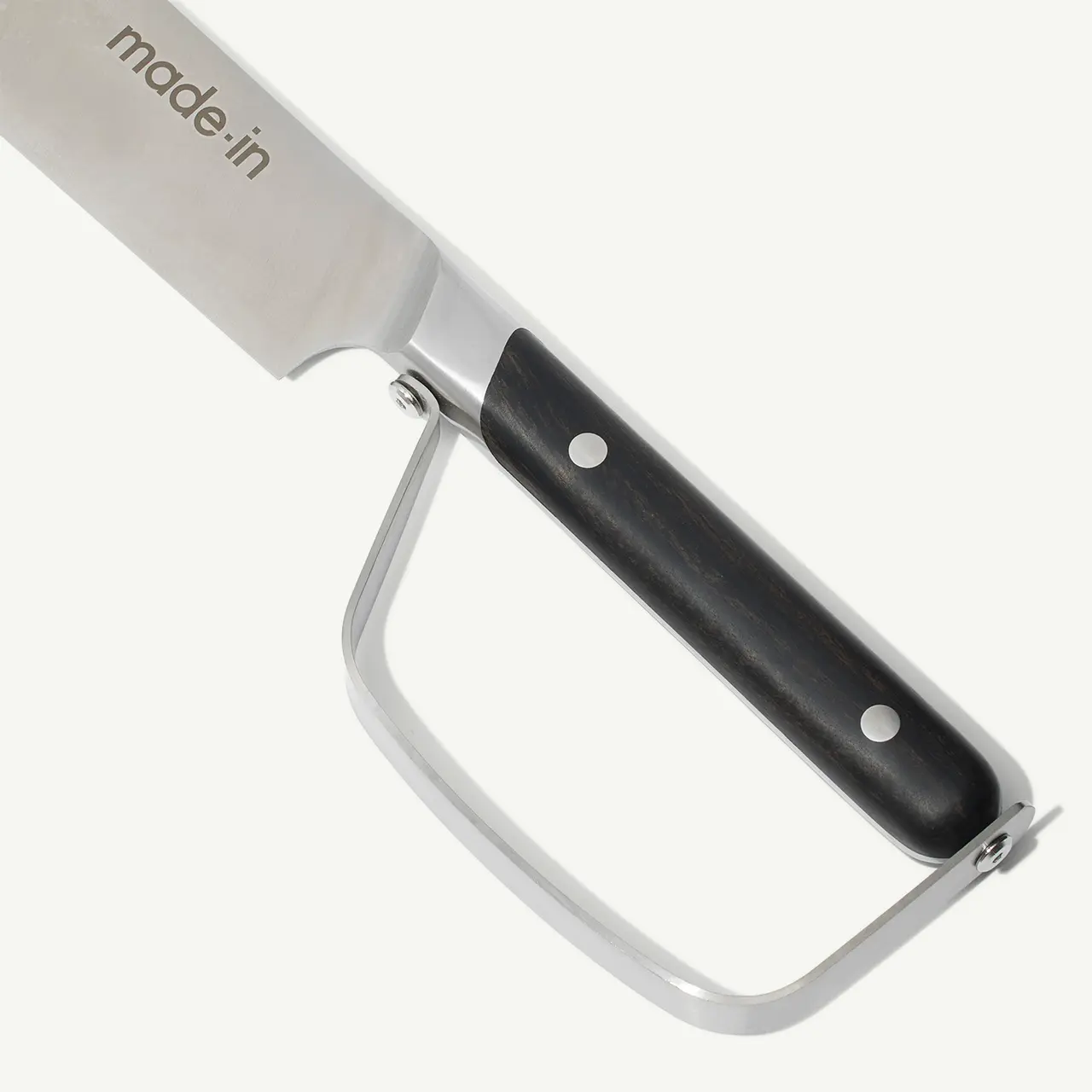 A close-up of a cheese slicer with a stainless steel blade and black handle against a white background.