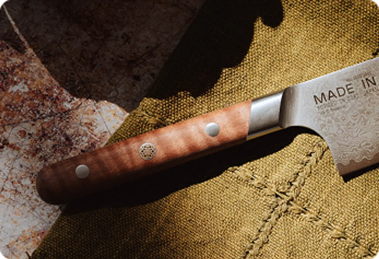 A beautifully crafted kitchen knife with a wooden handle and decorative blade rests on a textured, earthy-toned surface.
