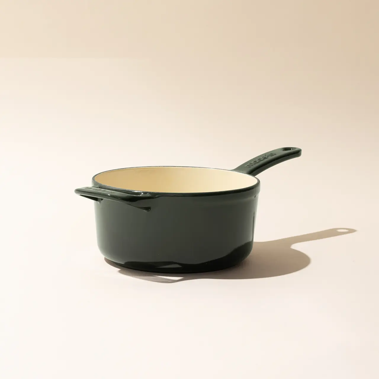 A dark green saucepan with a cream interior is centered on a neutral background, casting a soft shadow to the right.