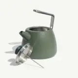 A modern green kettle sits beside a stainless steel lid and a long metal spout.