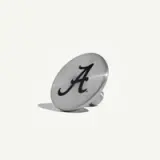 A circular metal button features a stylized black letter "A" on a brushed silver background.