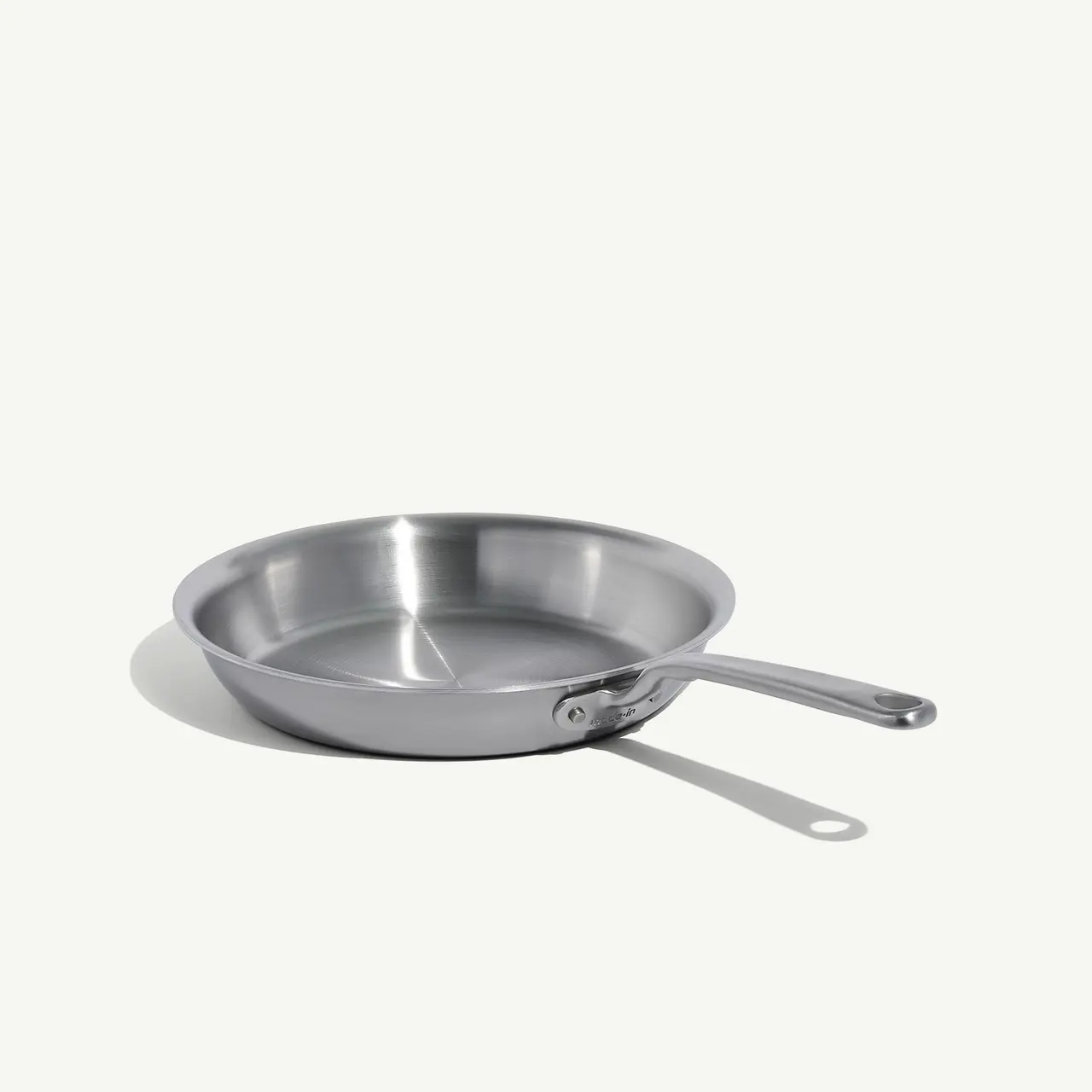 A stainless steel frying pan with a long handle is positioned on a light background.