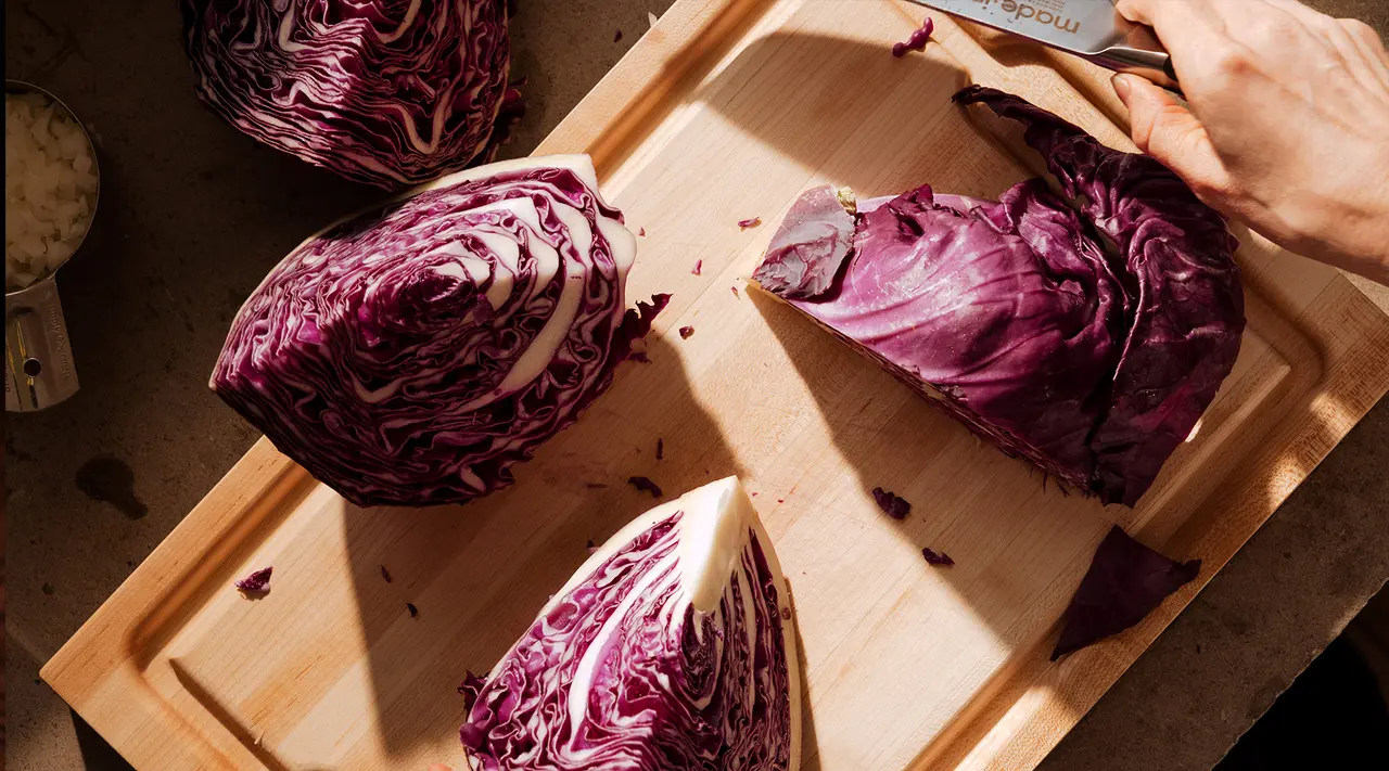A person is chopping red cabbage on a wooden cutting board, creating a vibrant contrast of colors and textures.