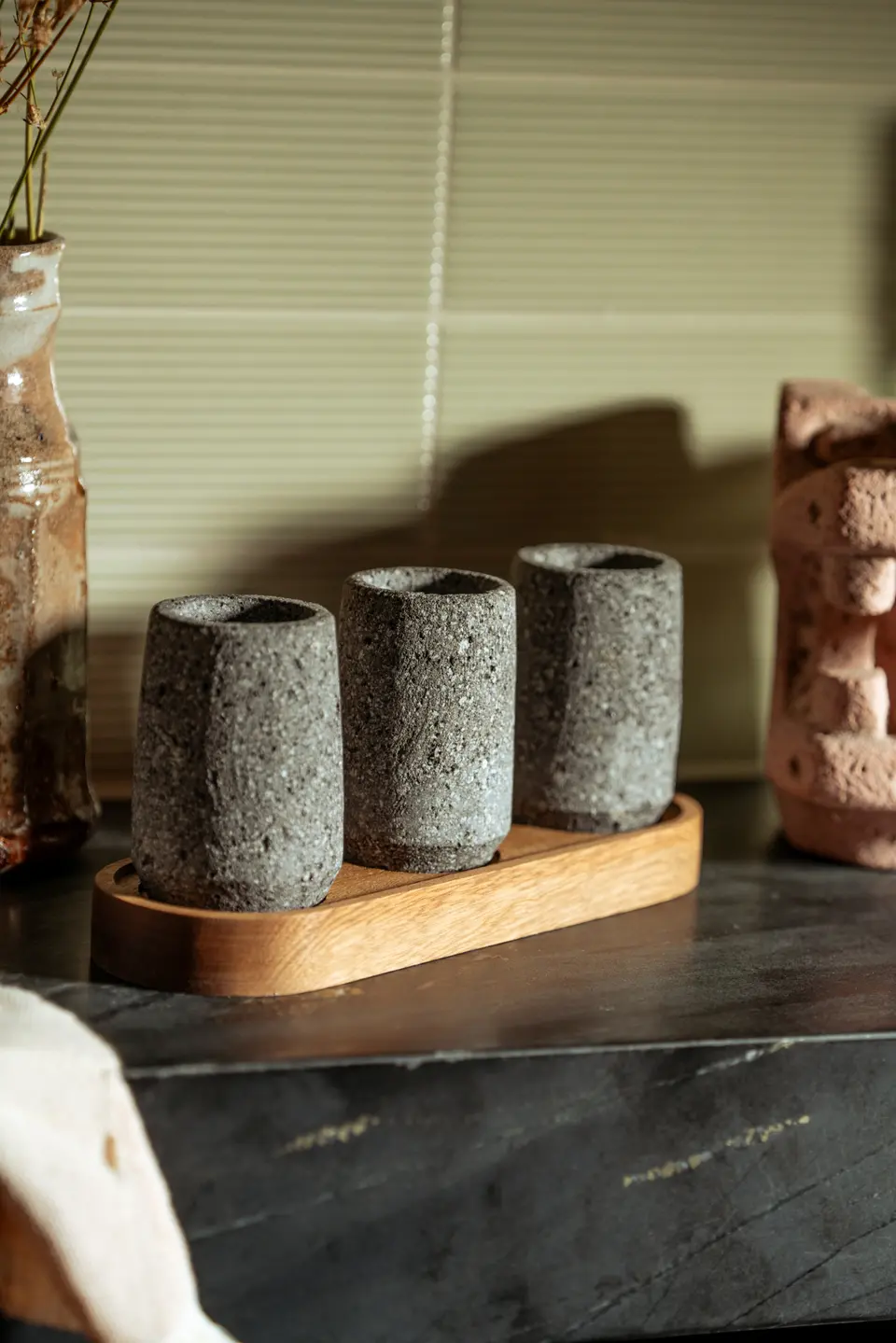 Four cylindrical concrete cups displayed on a wooden stand with decorative items in the background on a table.