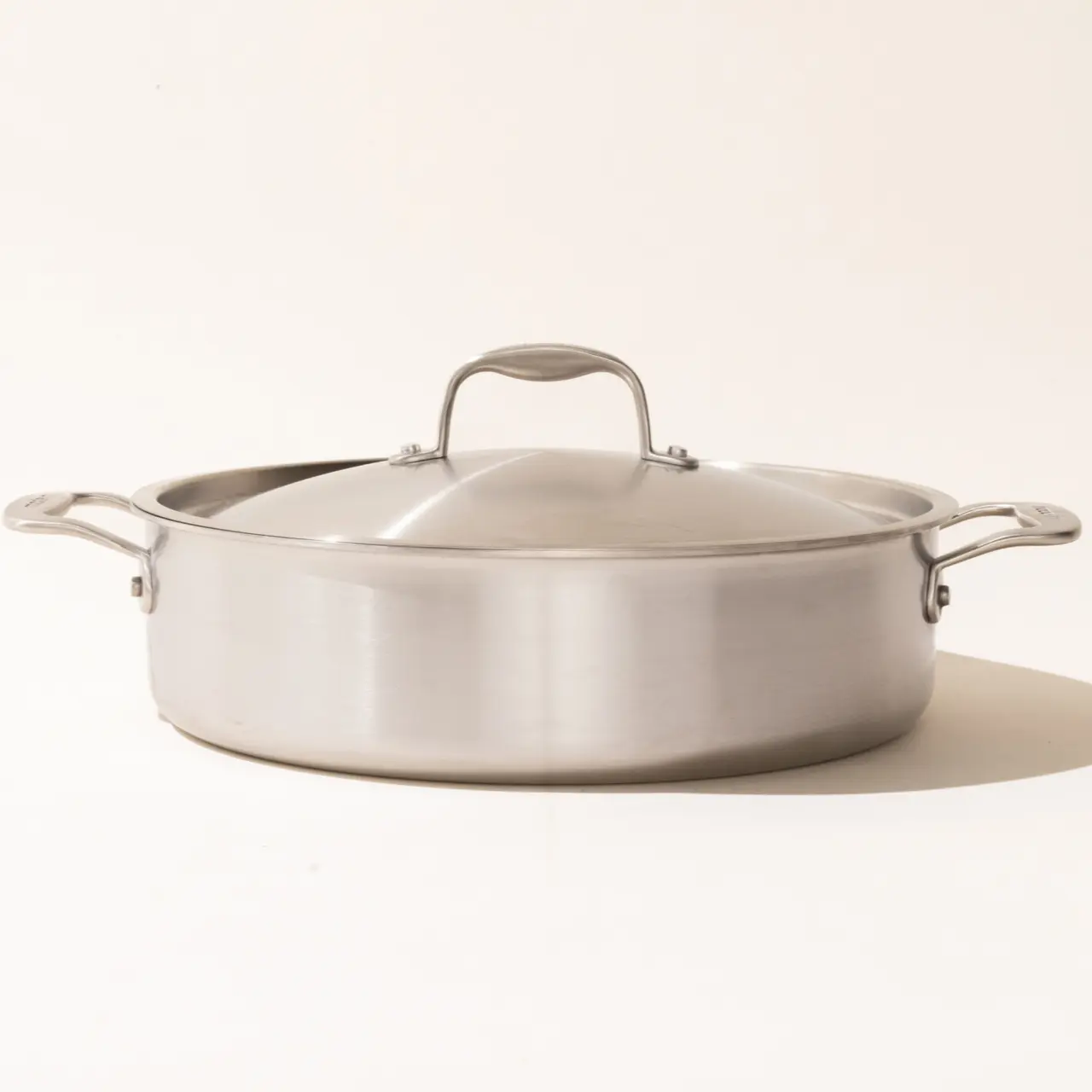 A stainless steel cooking pot with a lid and two handles against a light background.