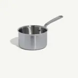 A stainless steel saucepan with a long handle sits isolated on a light background.