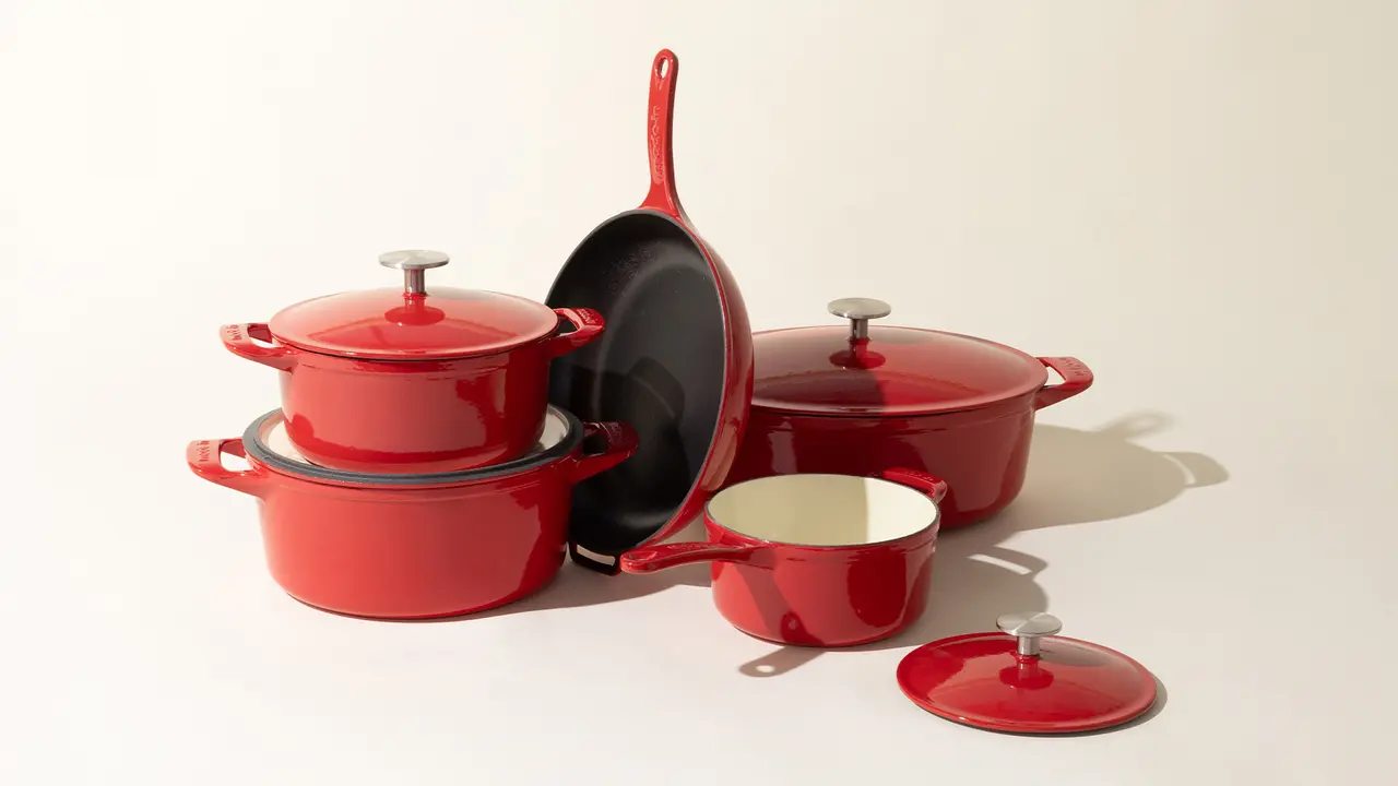 A set of red enameled cookware, including pots, a pan, and a lid, arranged on a light background.