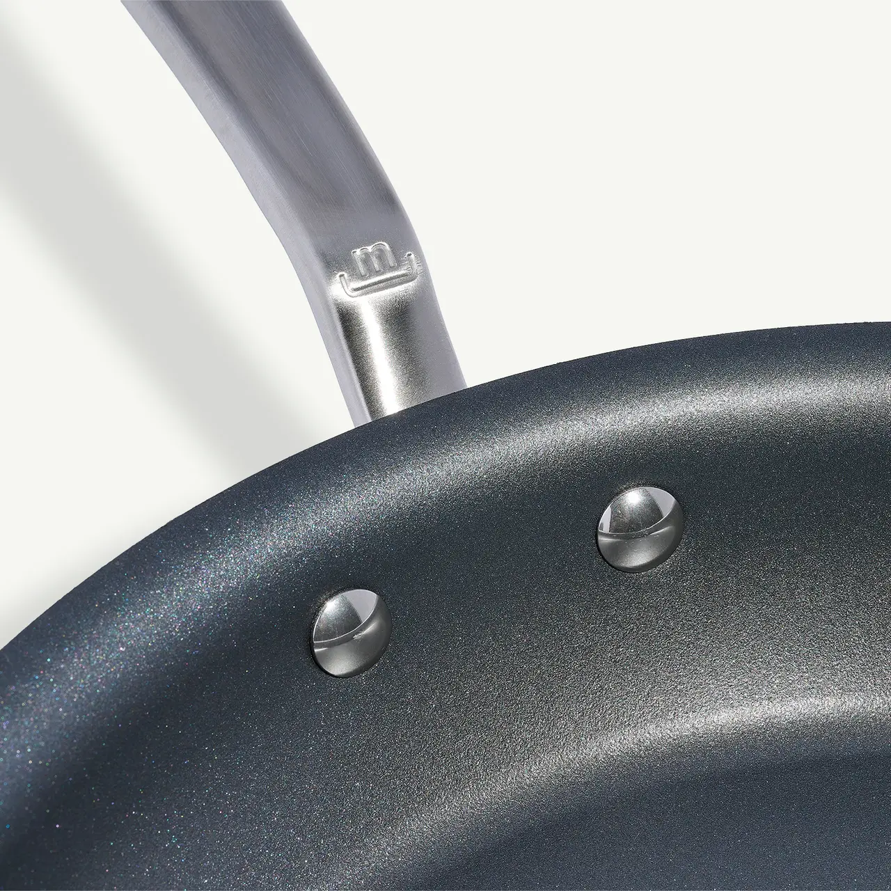 A close-up of a non-stick frying pan with its metallic handle visible, highlighting two rivets attaching the handle to the pan.