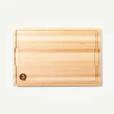 A wooden cutting board with a smooth surface and a decorative engraving in one corner.
