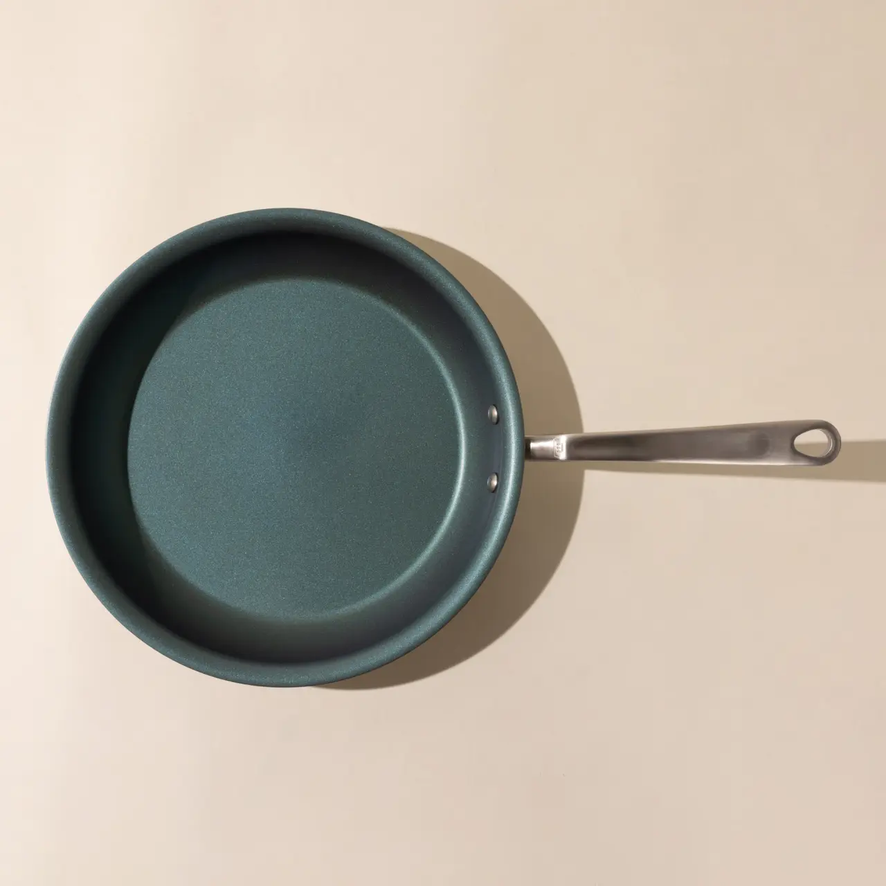 A new teal non-stick frying pan with a silver handle, viewed from above on a light surface.