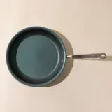 A new teal non-stick frying pan with a silver handle, viewed from above on a light surface.