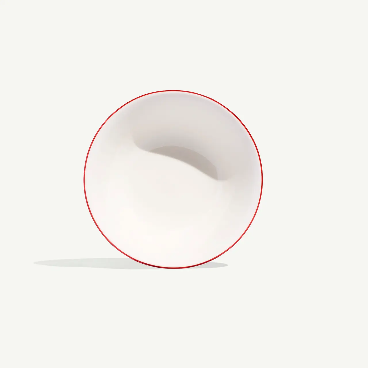 A white bowl with a red rim is tilted on a light background, casting a faint shadow.
