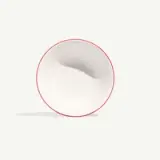 A white bowl with a red rim is tilted on a light background, casting a faint shadow.