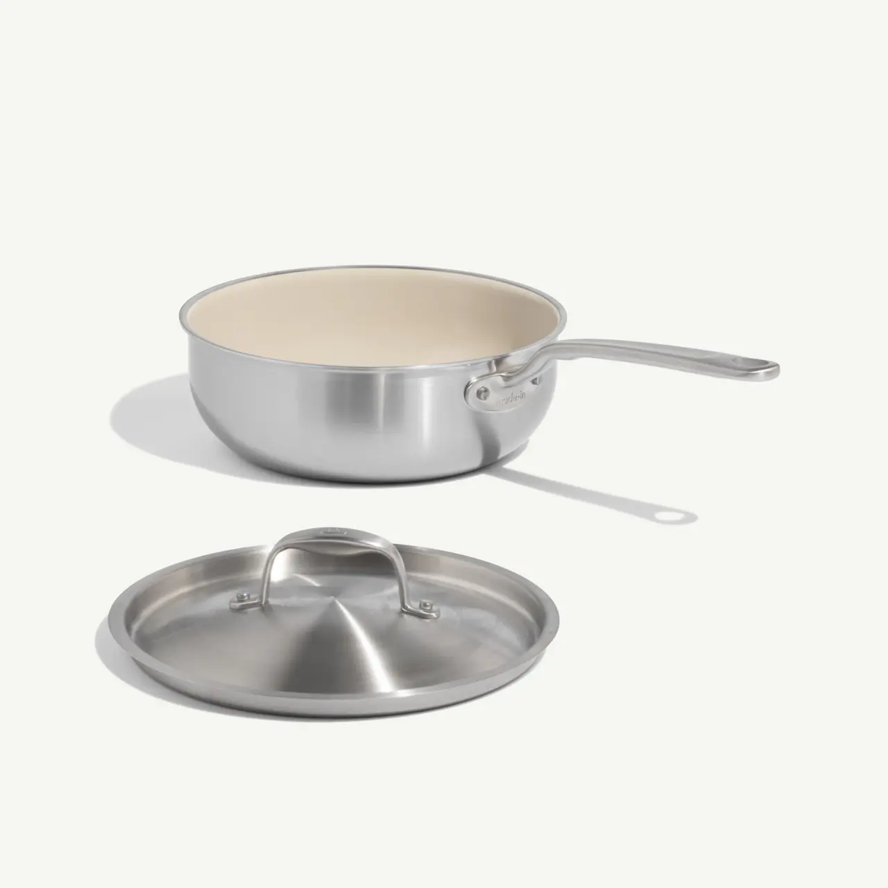 A shiny stainless steel saucepan with a beige interior and a matching lid rests beside it.