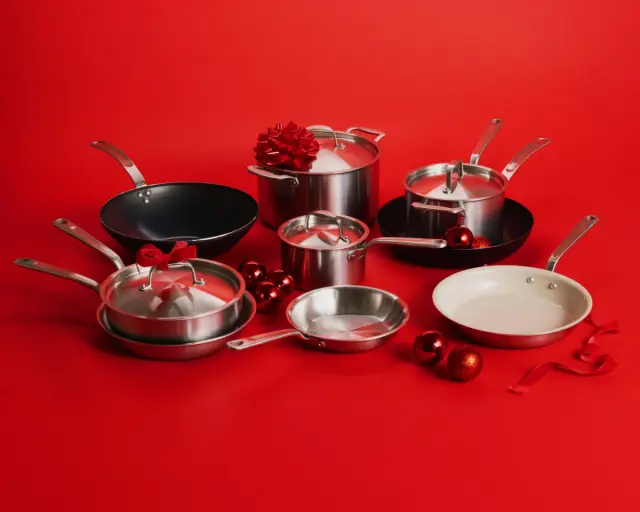 A collection of stainless steel cookware, including pots and pans, is arranged against a vibrant red background, adorned with festive decorations.