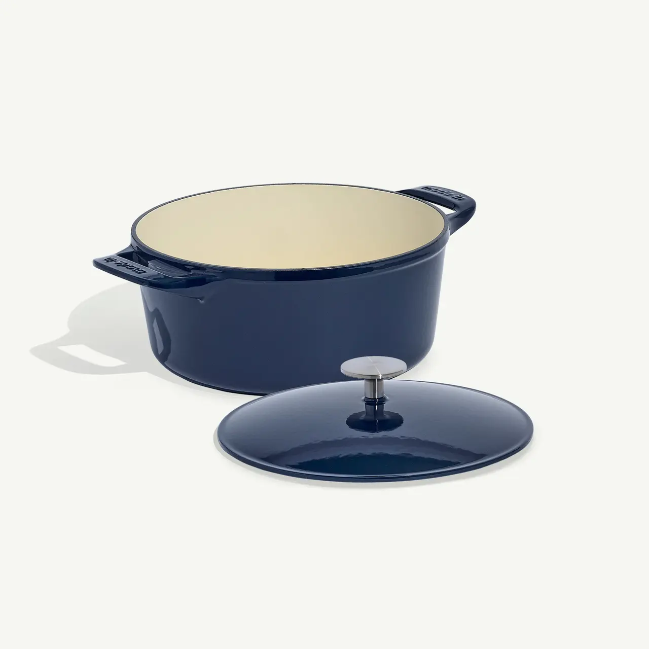 A navy blue dutch oven with its lid off to the side on a light background.