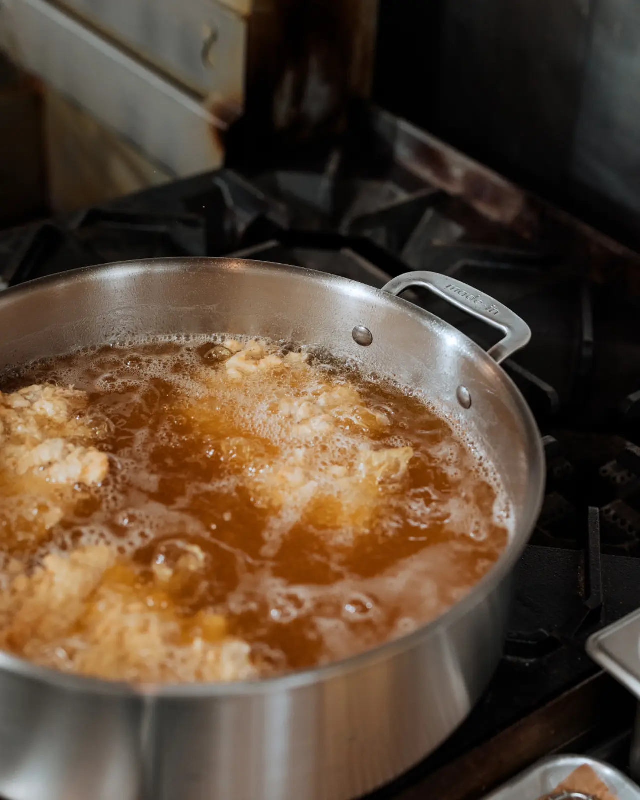 A large pot is simmering on the stove with golden-brown food items frying in bubbling oil.