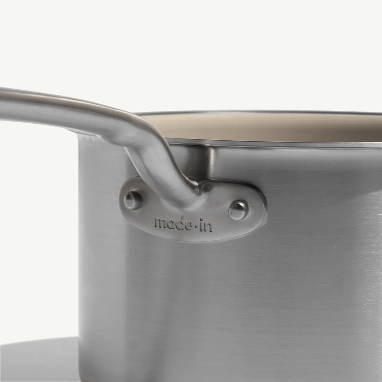 A close-up view of a stainless steel pot with a handle featuring the engraved brand name "mode-in."