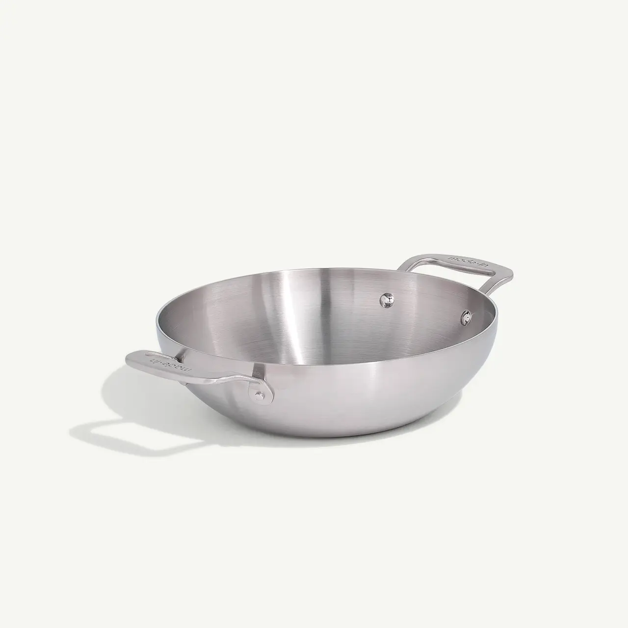 A stainless steel wok with two handles sits against a plain, light background.