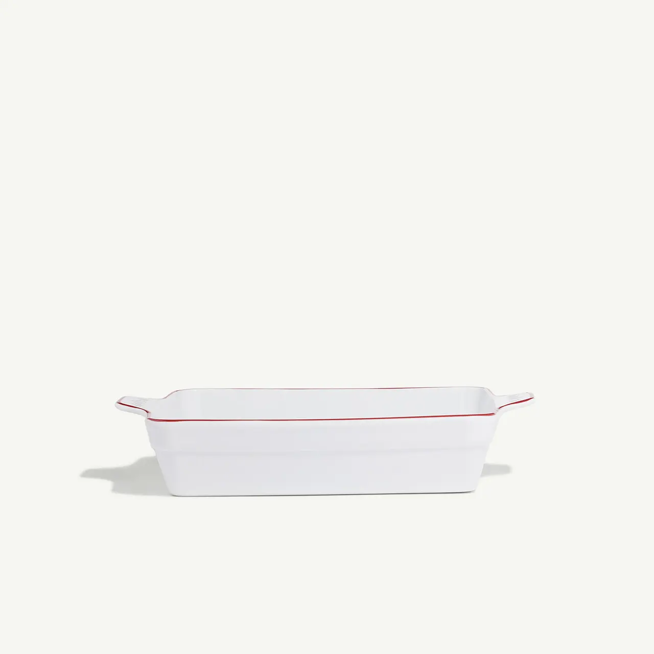 A white rectangular baking dish with red trim set against a plain background.