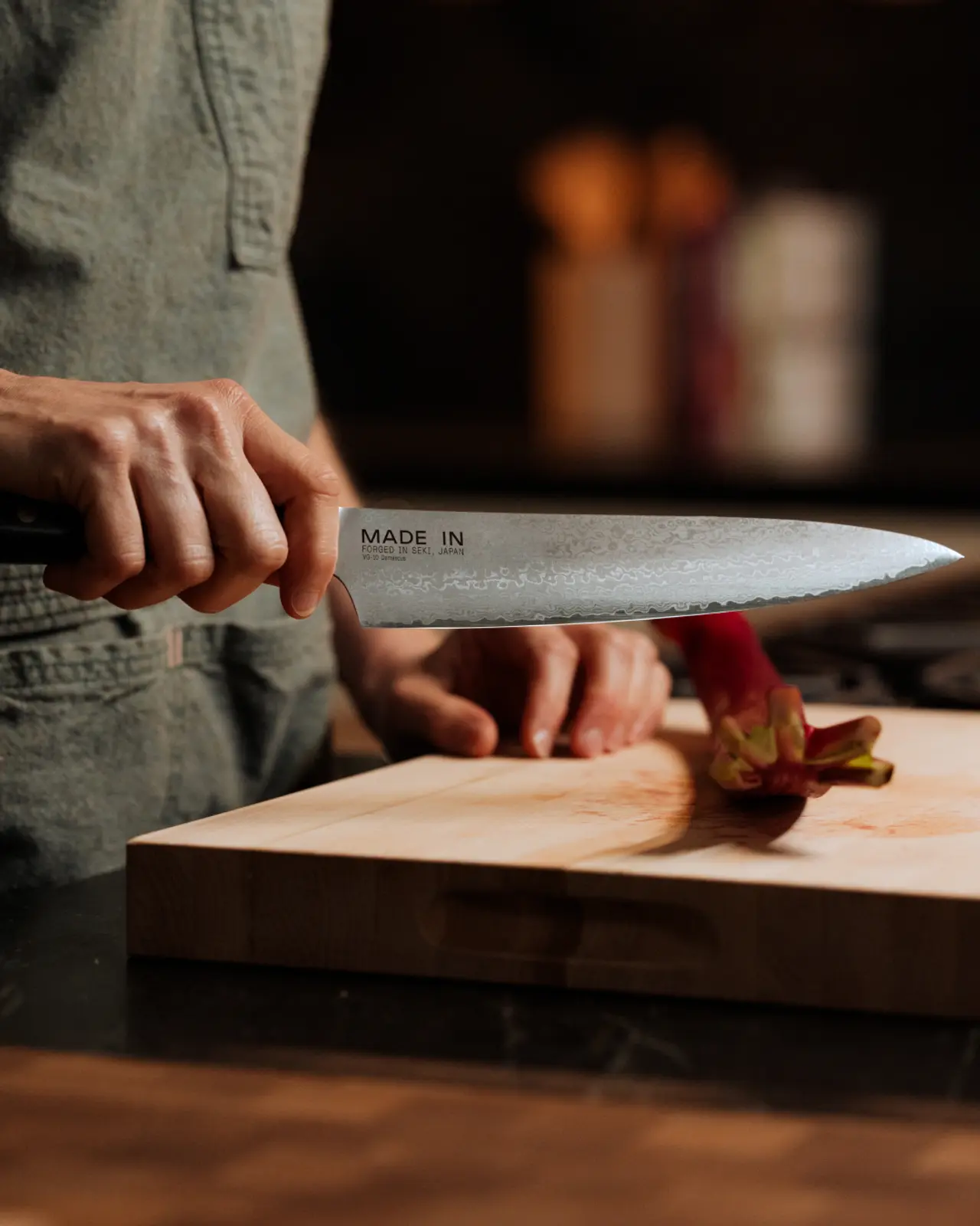 A person is holding a chef's knife above a cutting board with a partially sliced red vegetable on it.