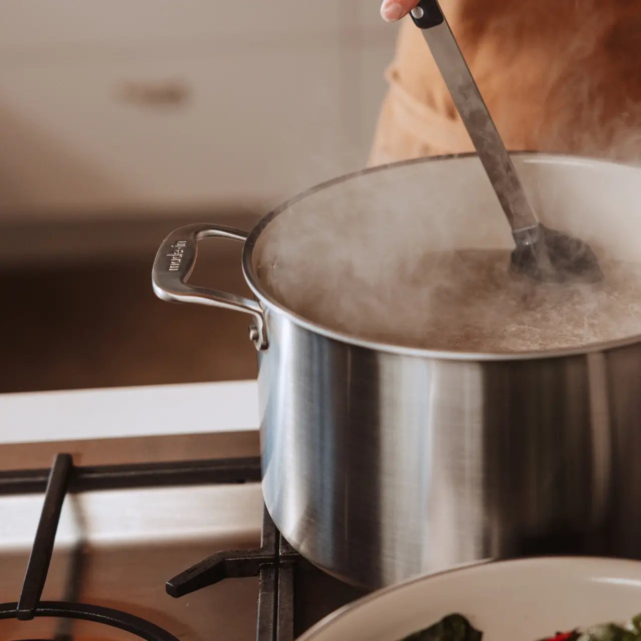 A person stirs a steaming pot on a stove, indicating active cooking.