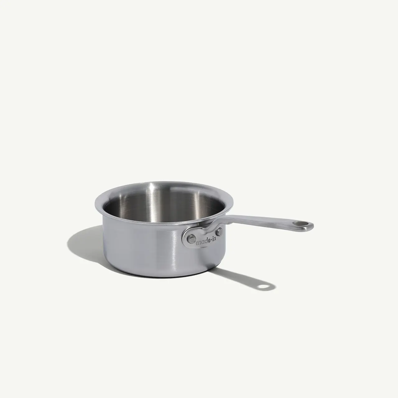 A stainless steel saucepan with a long handle sits on a plain, light-colored background.