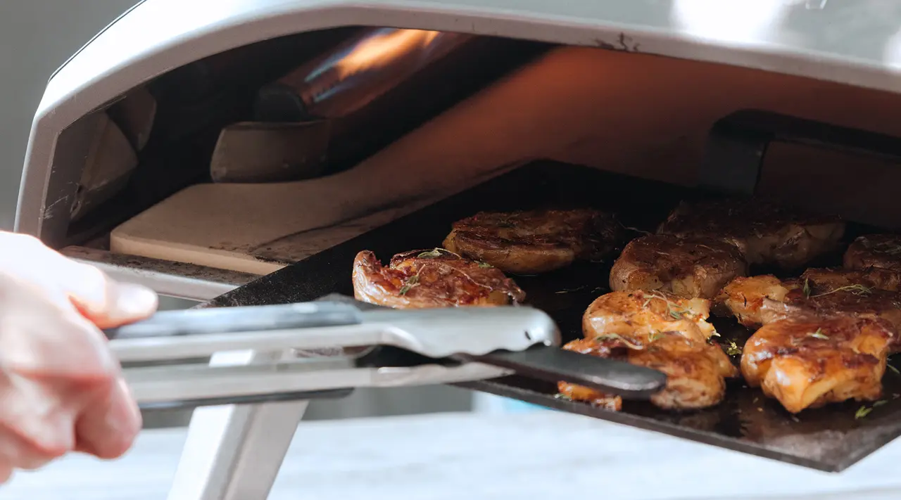 A person uses tongs to remove grilled chicken from a barbecue grill.