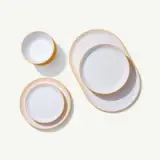 A neatly organized set of white plates and bowls with golden rims are arranged on a pale background.