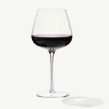 A stemmed wine glass filled with red wine sits against a neutral background with a light reflection visible on the surface.