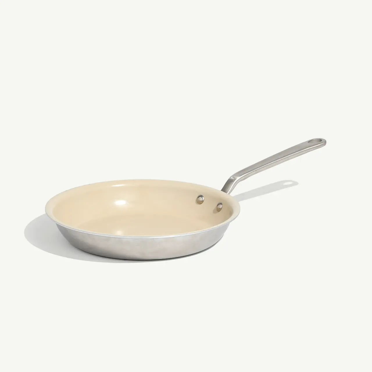 A stainless steel frying pan with a beige interior sits on a light background.