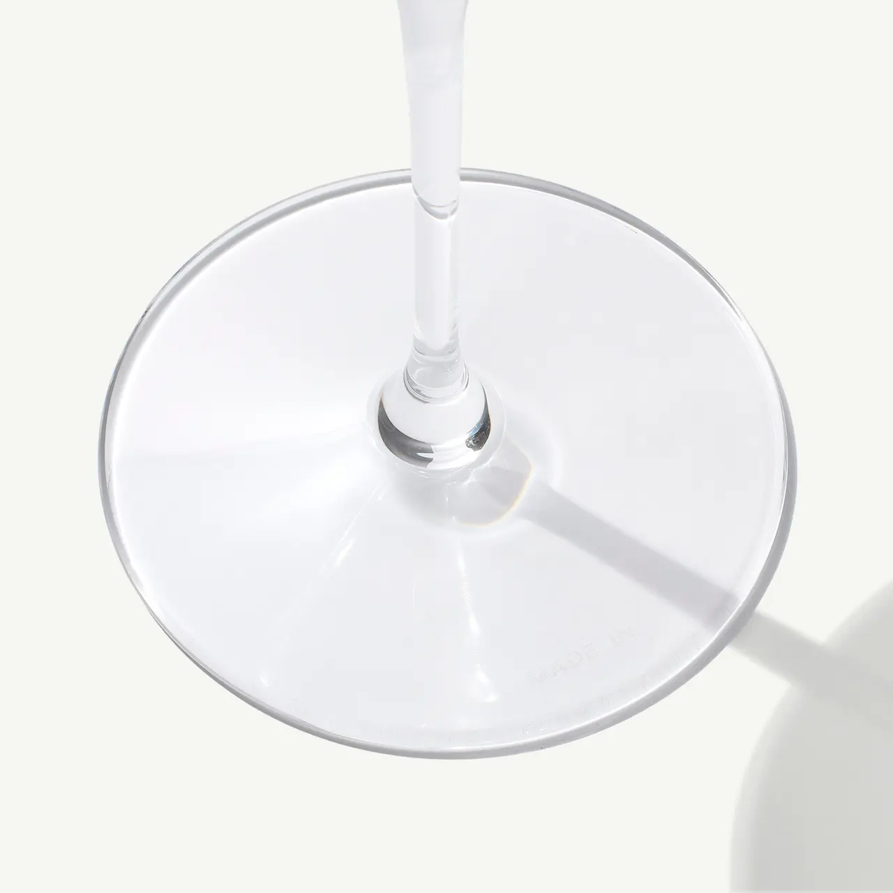 A wine glass casting a soft shadow on a plain surface under bright lighting, viewed from a top-down angle.