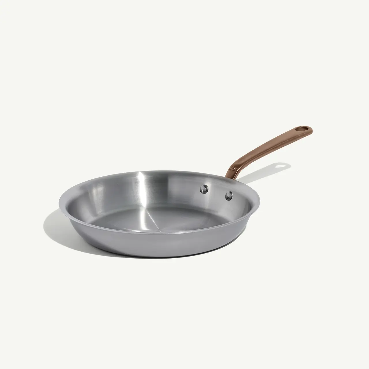 A stainless steel frying pan with a copper handle is positioned against a light background.