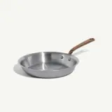 A stainless steel frying pan with a copper handle is positioned against a light background.