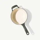 A round, two-toned cooking pot with a dark green exterior and a light beige interior.