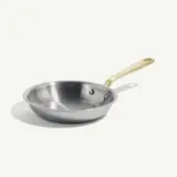 A stainless steel frying pan with a gold-colored handle is placed against a plain background.