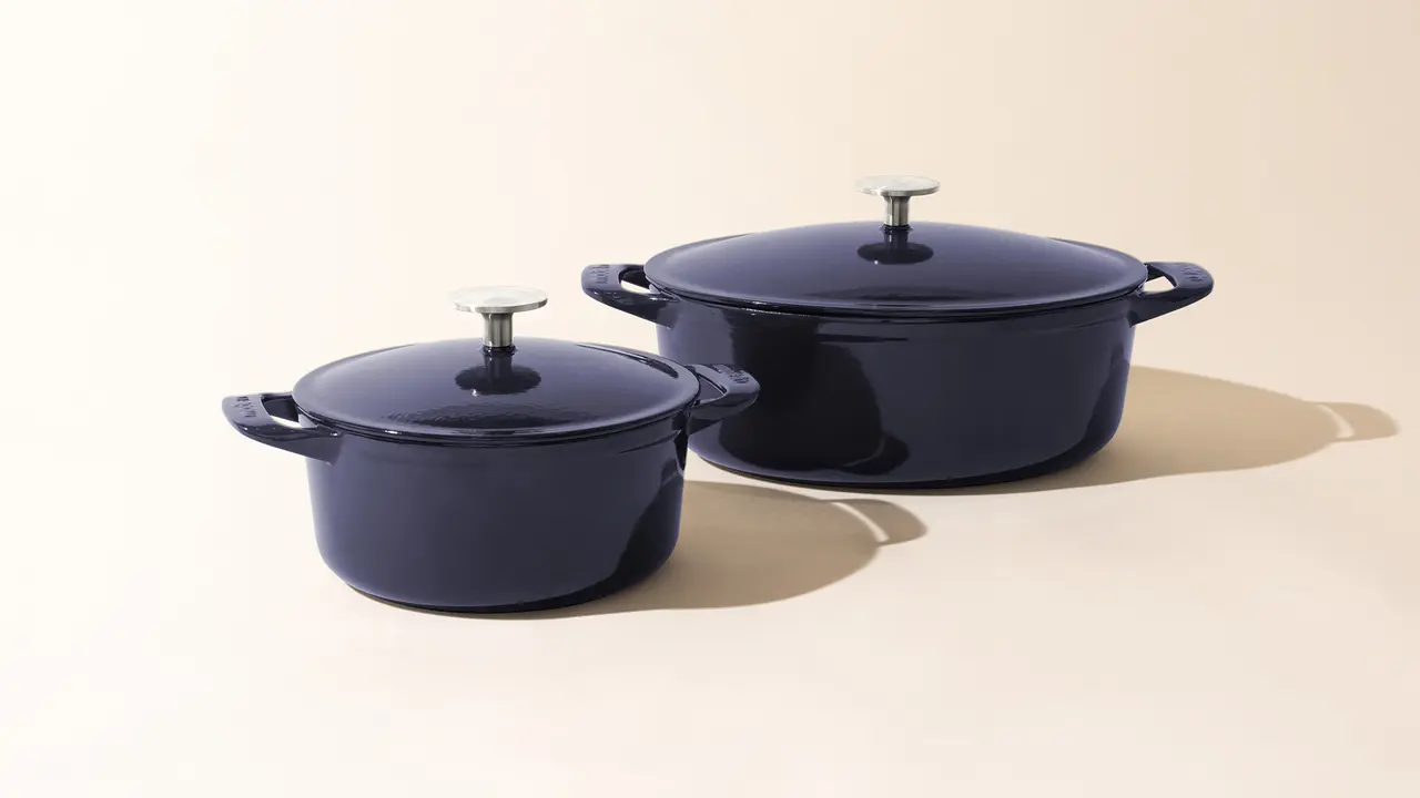 Two blue enameled cast iron Dutch ovens, one smaller than the other, with lids on, sitting against a light background.