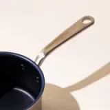 A new, clean saucepan with a stainless steel handle casting a shadow on a neutral background.