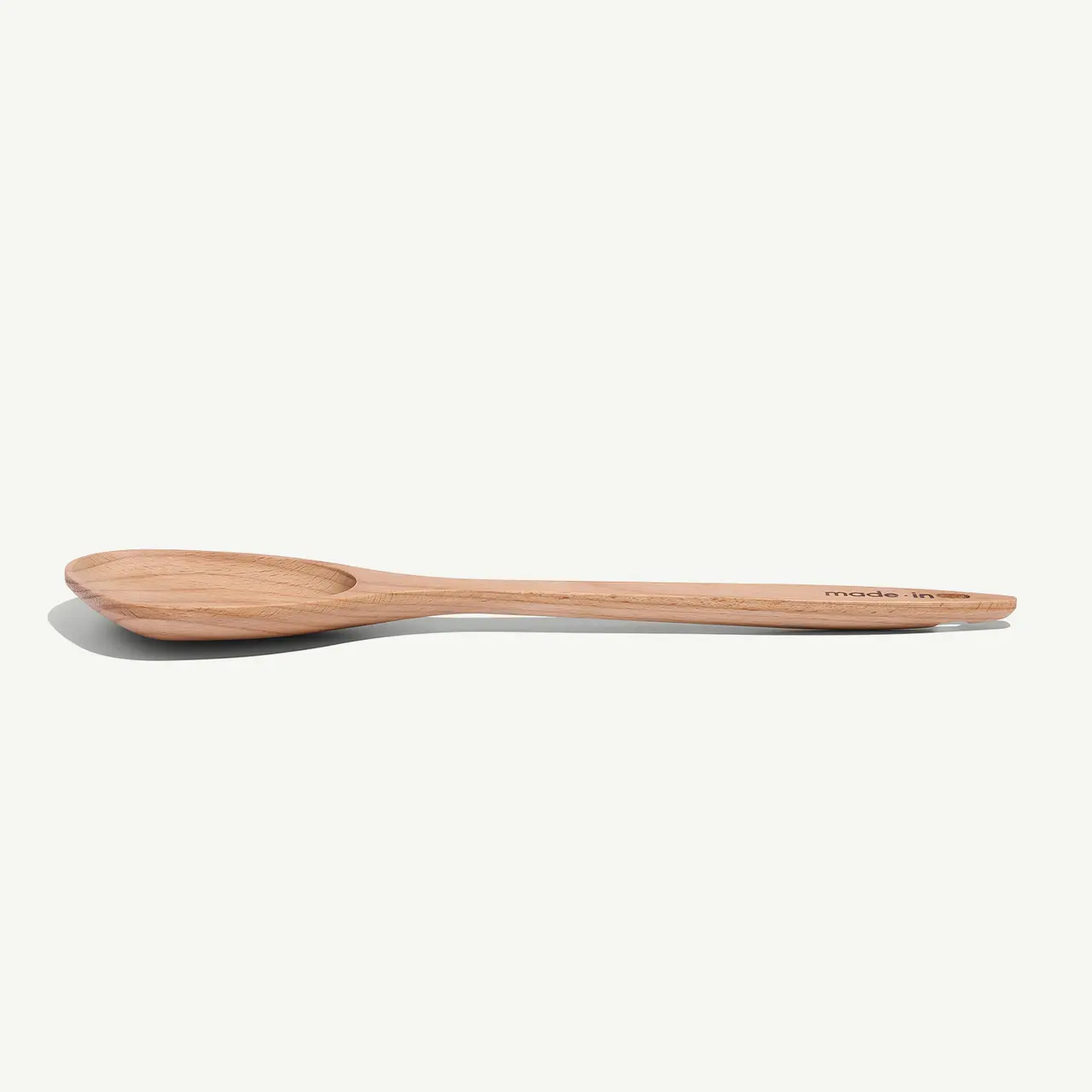 A simple wooden spoon lies horizontally against a plain white background.