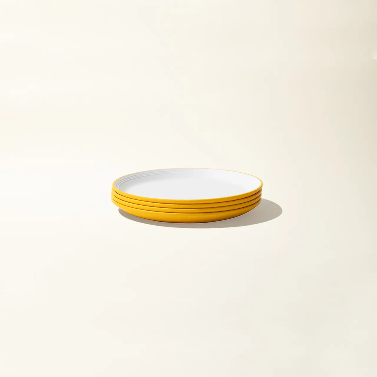 A stack of clean, white plates with yellow rims sits on a pale background.