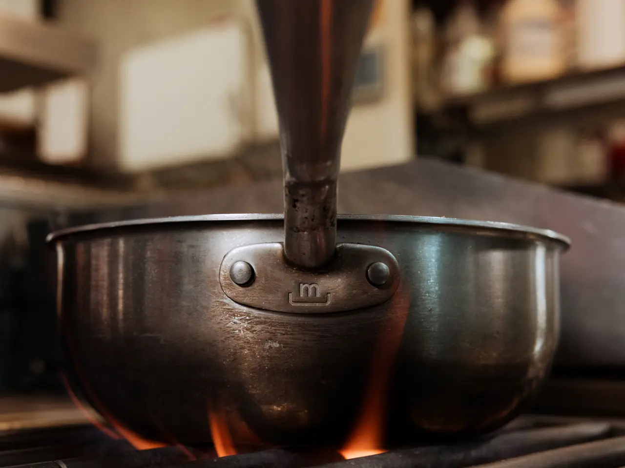 Close-up of a metal cooking pot on a gas stove with flames licking the bottom.
