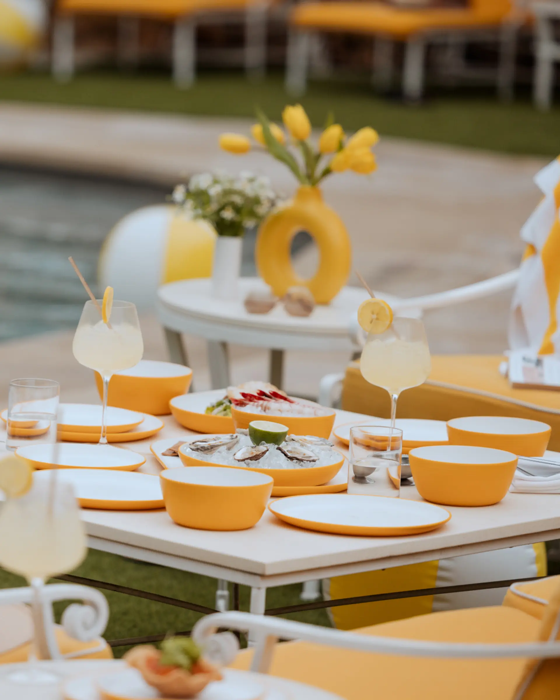 A neatly arranged outdoor dining table features a yellow color theme with matching dishes, glasses, and decorative elements.