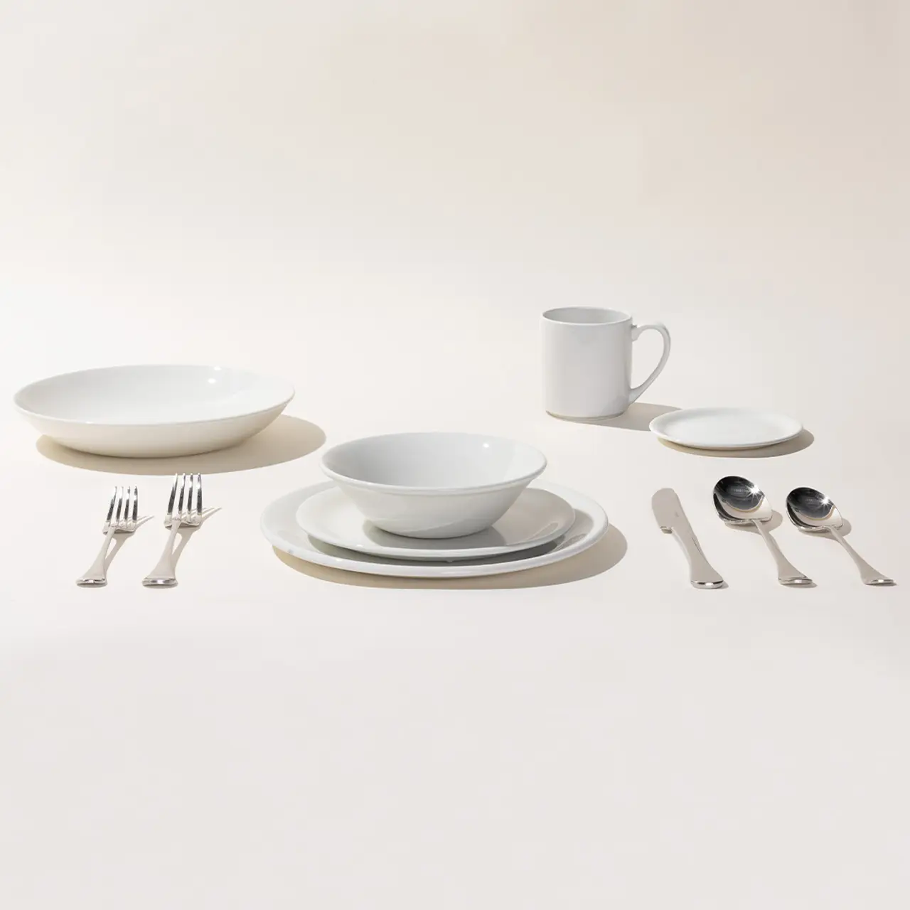 A neatly arranged set of white dinnerware and silver cutlery is displayed against a light background.