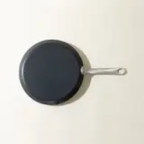 A non-stick frying pan with a long handle is placed on a light-colored surface, viewed from above.
