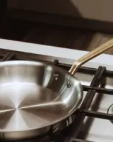 A stainless steel frying pan rests on a gas stove burner with its handle extending to the right.