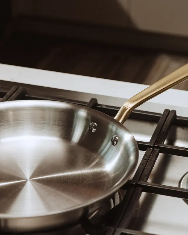 A stainless steel frying pan rests on a gas stove burner with its handle extending to the right.